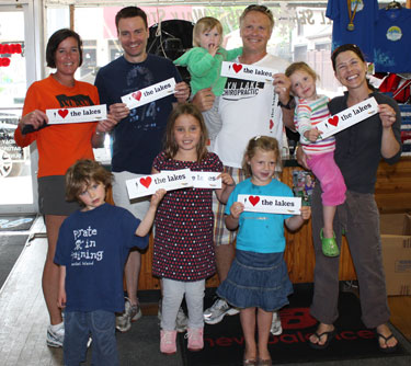 Group of Lyn Lake Chiropractic patients and family members posing indoors holding "I heart the lakes" signs while wearing Lyn Lake Chiropractic t-shirts